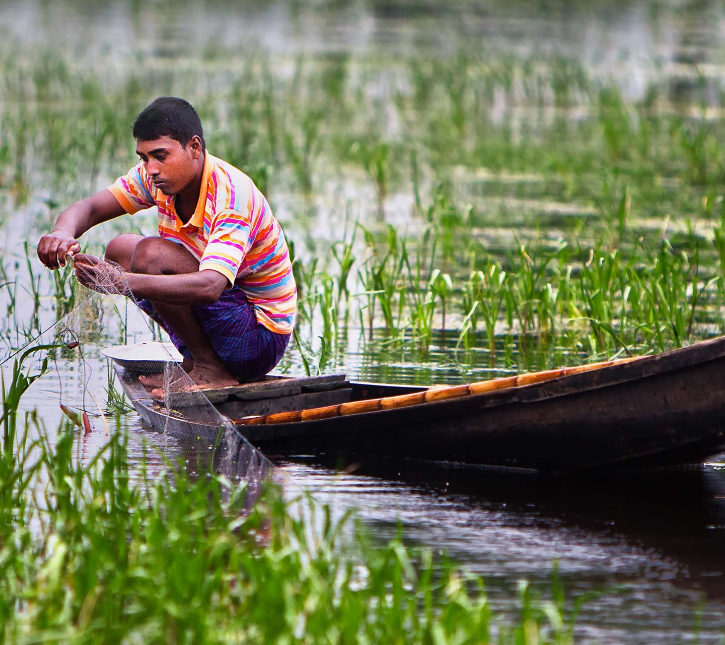 Young south Asian man fishing on a canoe with a net